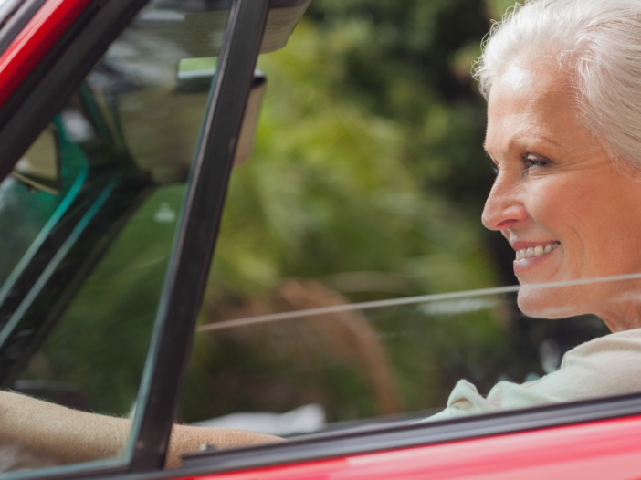 A smiling woman confidently driving a red car, symbolizing forward movement and success in crafting content that converts in marketing strategies.